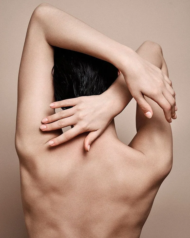 la imagen muestra a una persona sin ropa, de espaldas tocándose el cuello con la mano derecha