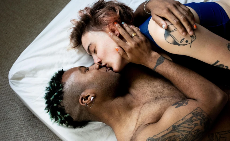 Hombre y mujer con tatuajes besándose en la cama