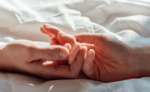 Dos manos en una cama agarrándose mutuamente